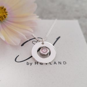 Barnhalsband med en cirkel i silver där det hänger en månadsstens berlock